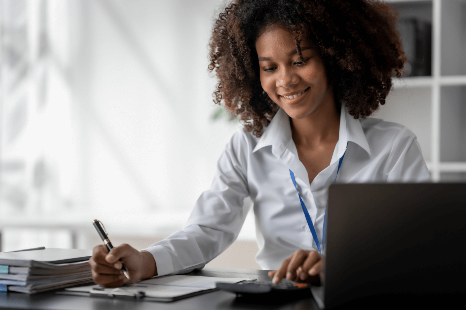 Jovem com óculos sorri enquanto trabalha em seu laptop, refletindo a inovação na administração de prédios e melhorias.
