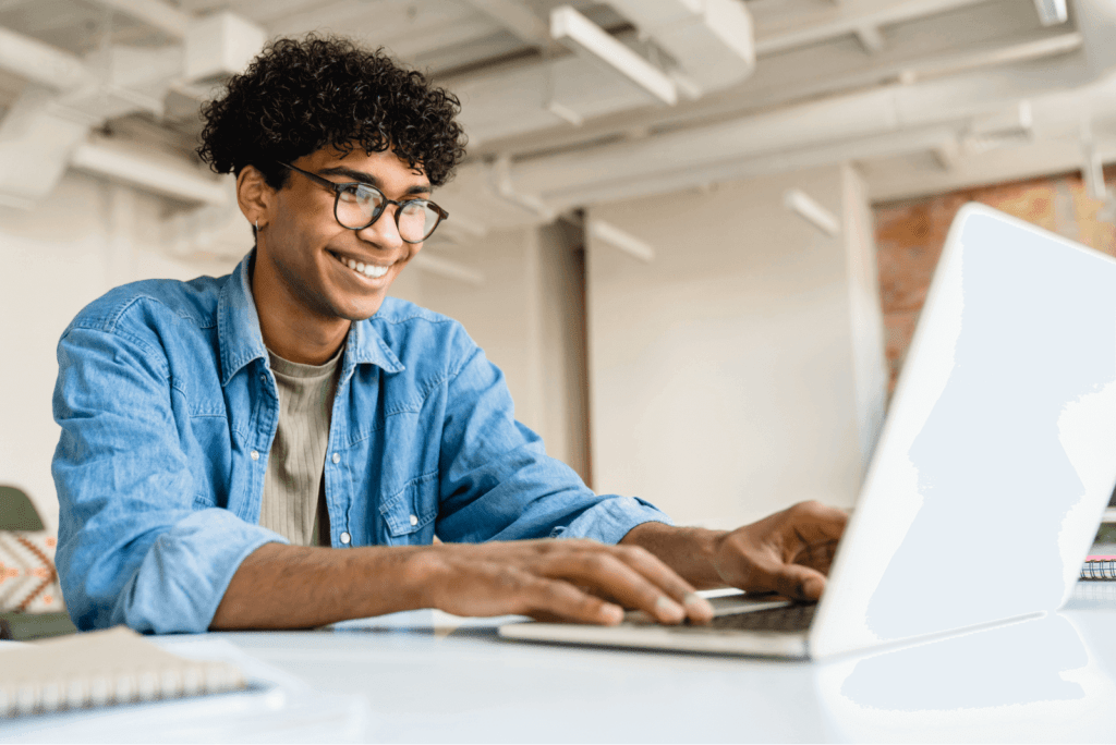 Jovem com óculos sorri enquanto trabalha em seu laptop, refletindo a inovação na administração de prédios e melhorias.